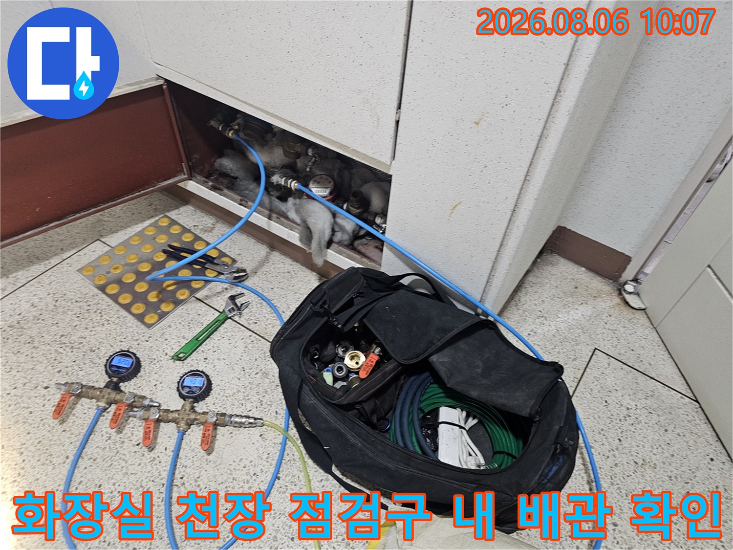 화장실 천장 점검구를 통해 노출된 배관과 압력 체크 장비가 있는 모습