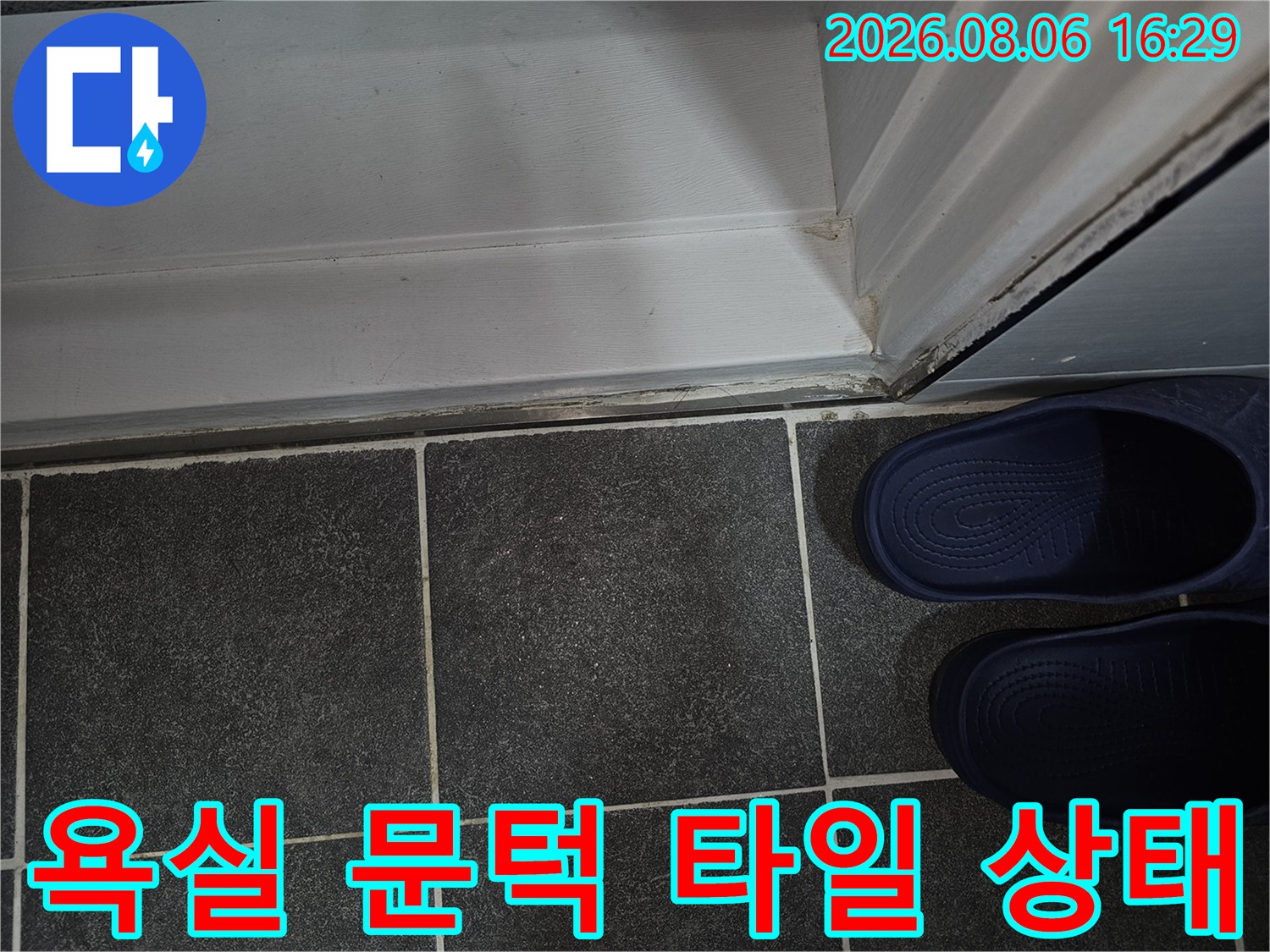어두운 색상의 욕실 타일과 밝은색 문틀 경계면의 마감 상태를 보여줍니다.