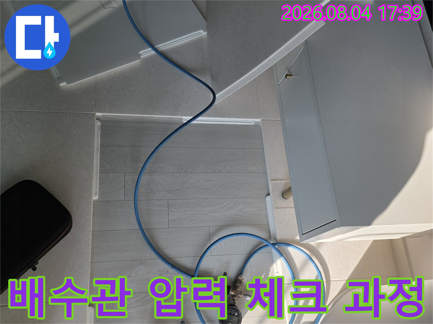 긴 파란색 호스와 게이지를 연결하여 배수관 내부에 막힌 구간이 있는지 확인하는 전문 점검 장면.