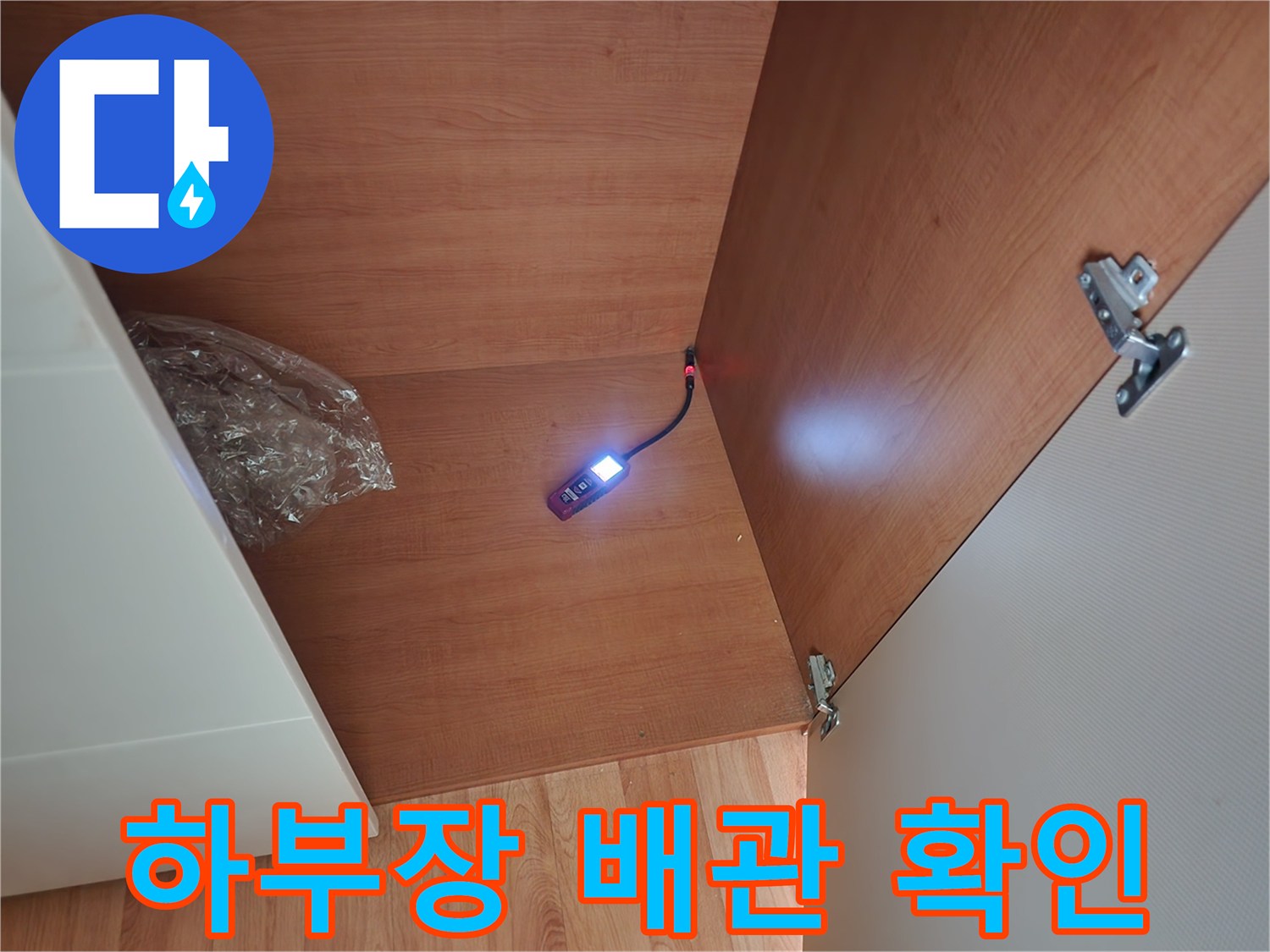 싱크대 밑 어두운 공간의 배관 부위를 조명으로 비추는 모습