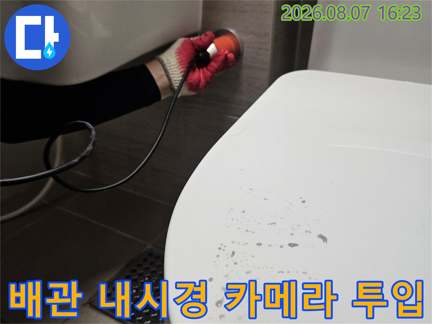 장갑을 낀 작업자가 변기 근처에서 내시경 장비를 조작하는 장면