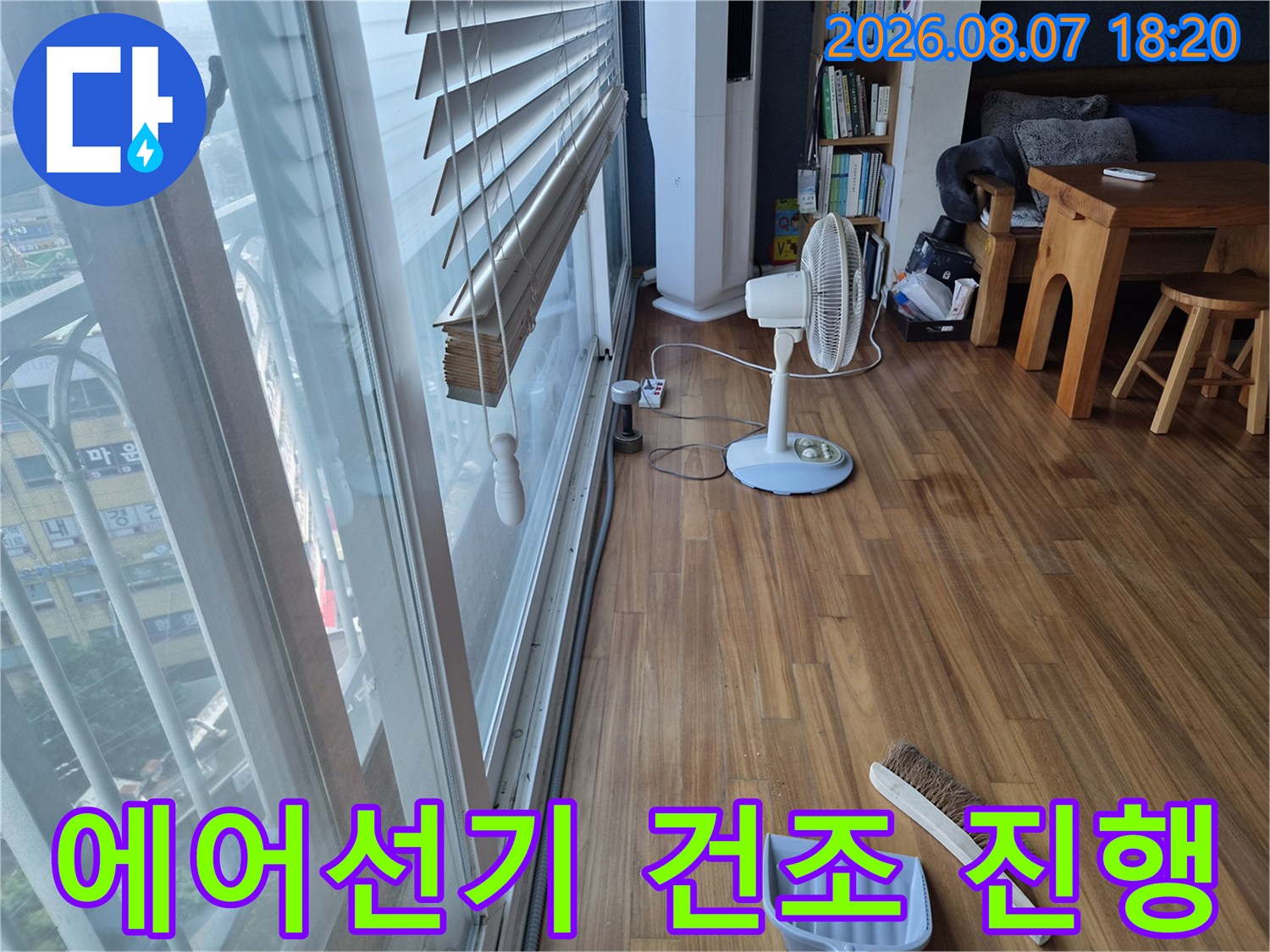 선풍기를 가동하여 누수 발생 부위의 바닥을 말리고 있는 거실 내부 사진입니다.
