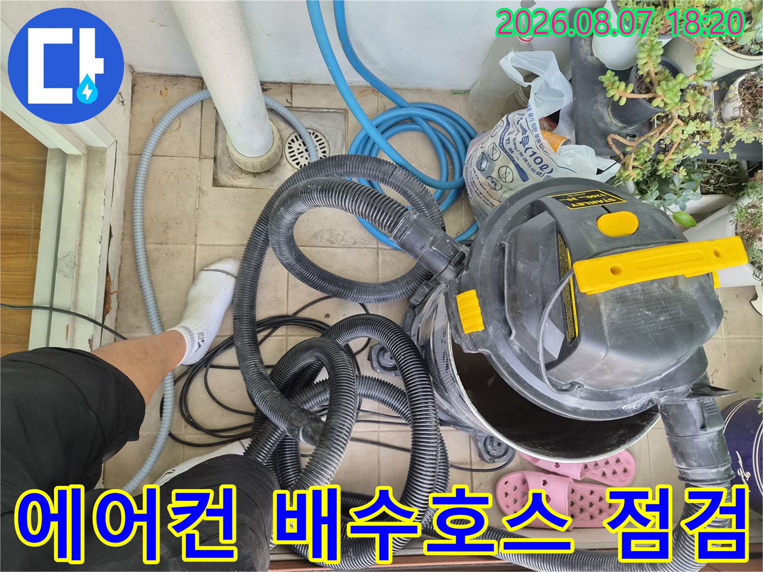파란색 호스와 대형 청소 장비가 놓여 있는 에어컨 배수관 작업 현장입니다.