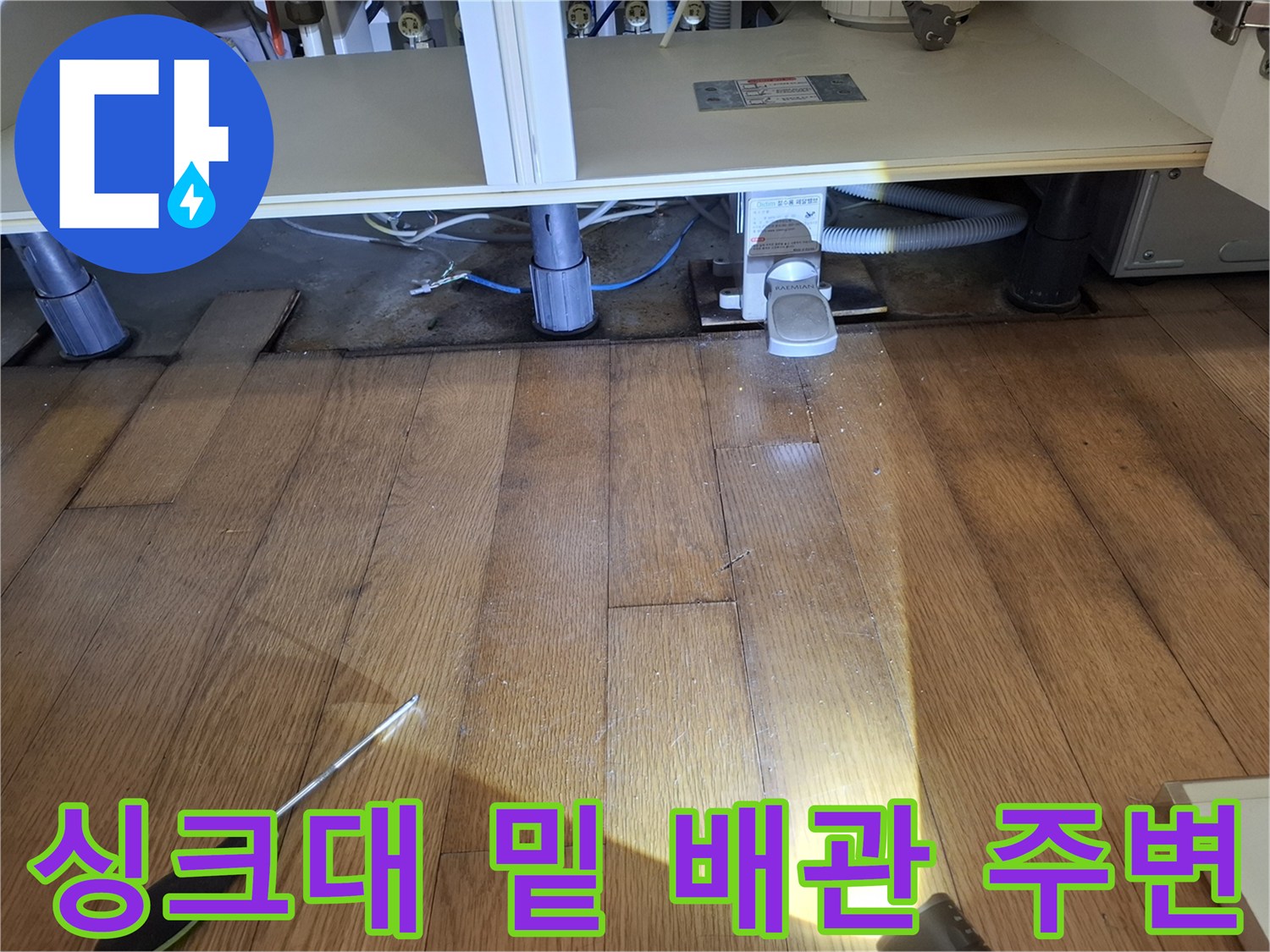 싱크대 하단 배관 부근의 젖은 마루와 드라이버가 놓인 현장입니다.