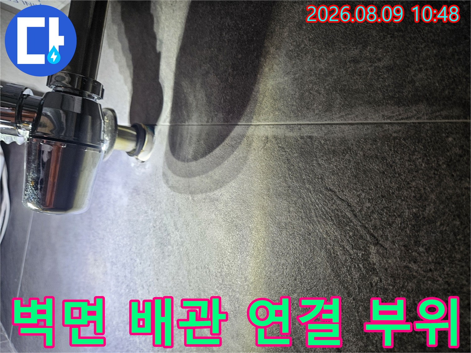 어두운 질감의 타일과 밝은 크롬 배관의 경계 부분