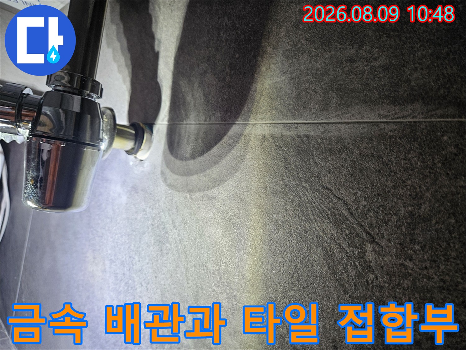 어두운 회색 타일 벽면에 설치된 금속제 배관 연결 부위