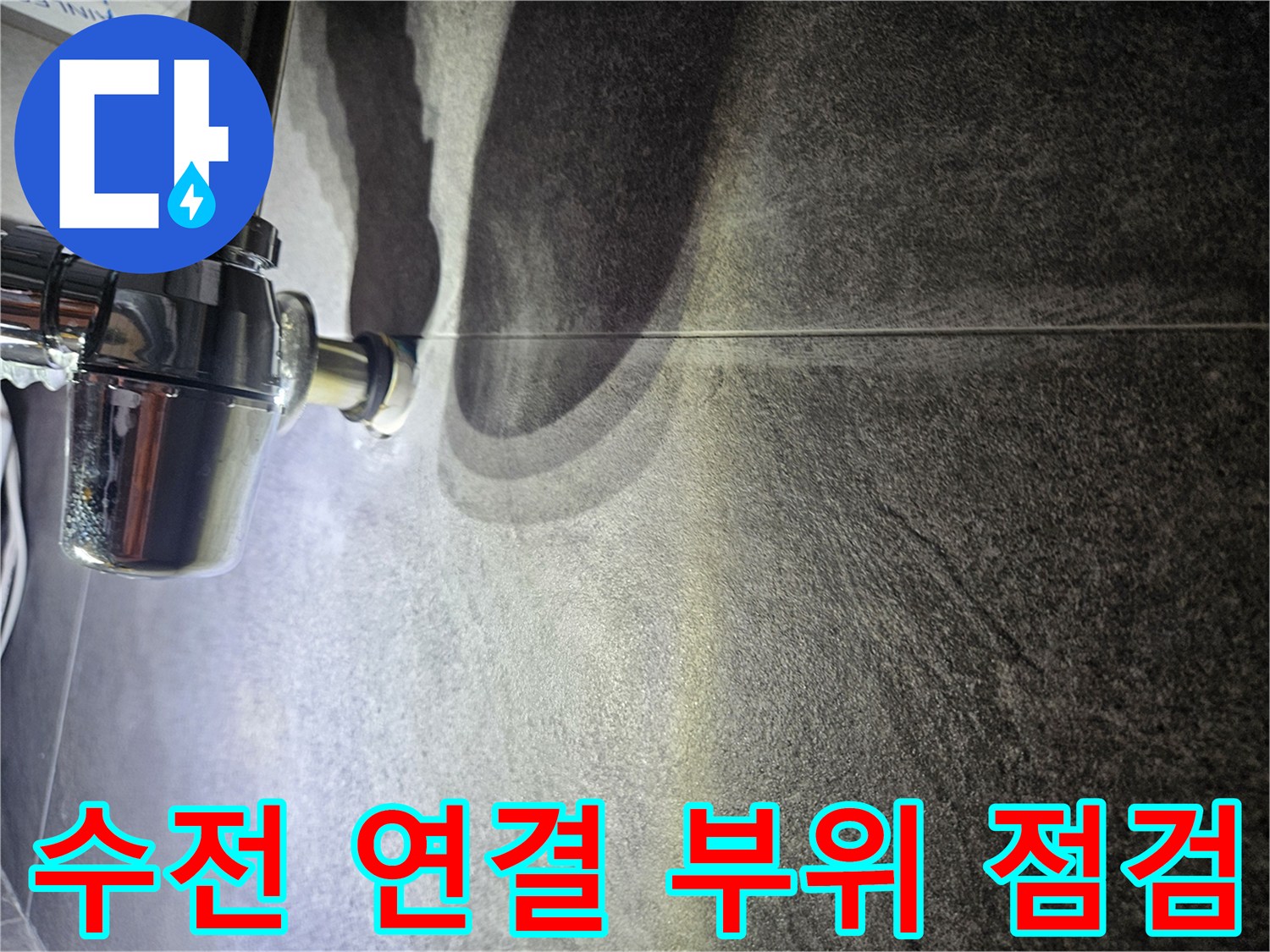 어두운 회색 타일 벽면의 크롬 배관 연결 지점 상세 촬영