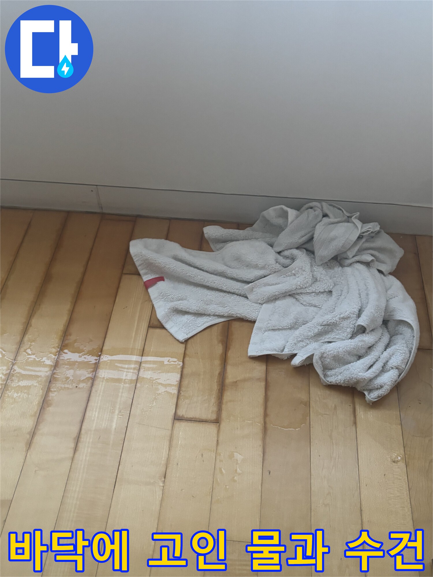 나무-바닥재-위에-물이-고여-있고-그-옆에-흰색-수건이-놓여-있는-모습