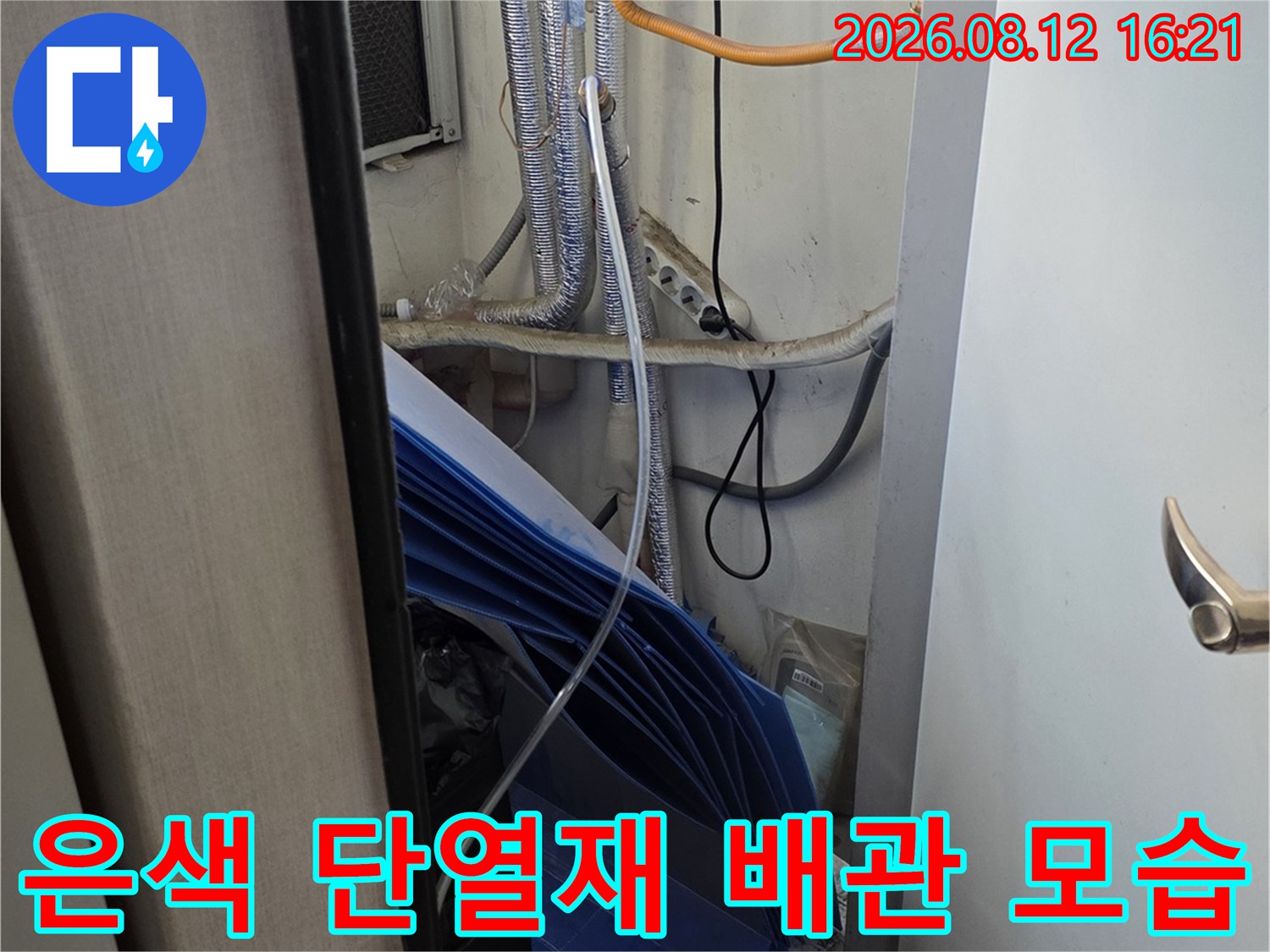 보일러 하단에 설치된 은색 보온재 마감 배관과 노란색 전기선-파란색 구조물 일부