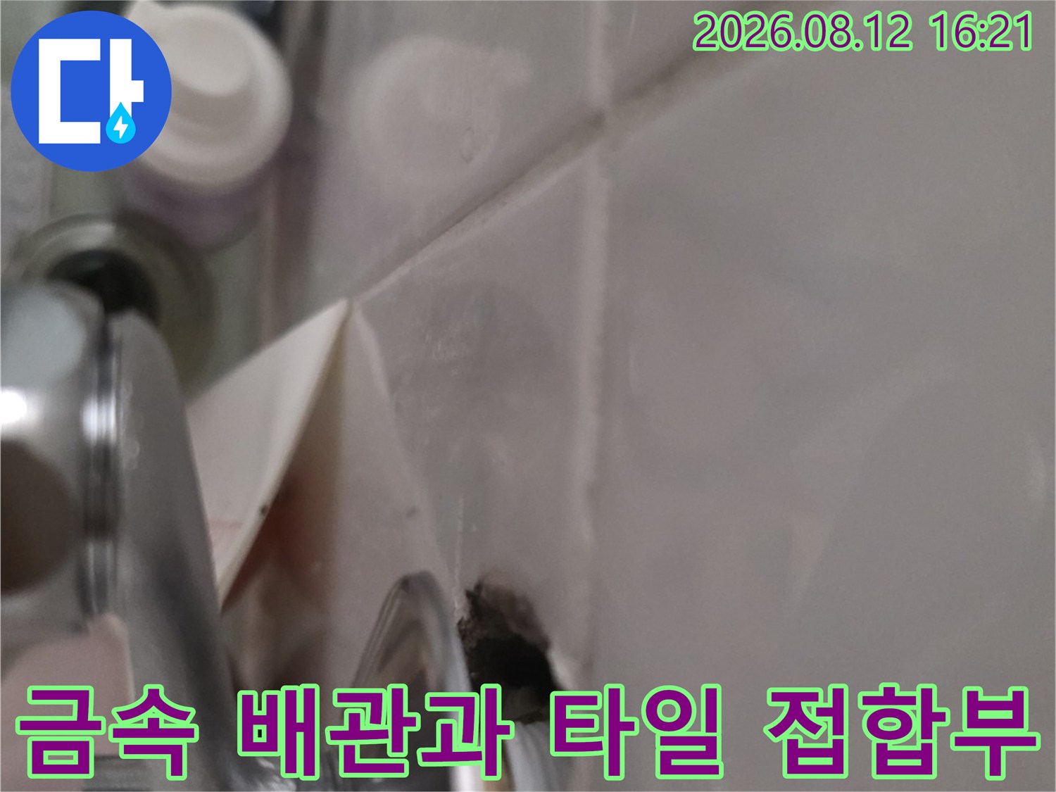 은색 세면대 배관이 화장실 벽면 타일에 연결된 부위의 파손 상태-근접 촬영