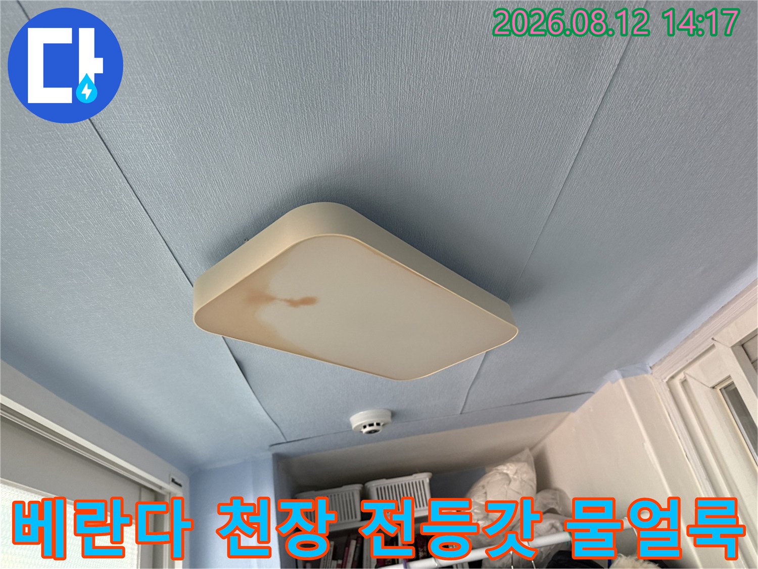 하늘색 베란다 천장에 설치된 사각형 조명 덮개 가장자리에 갈색 누수 얼룩이 생긴 모습