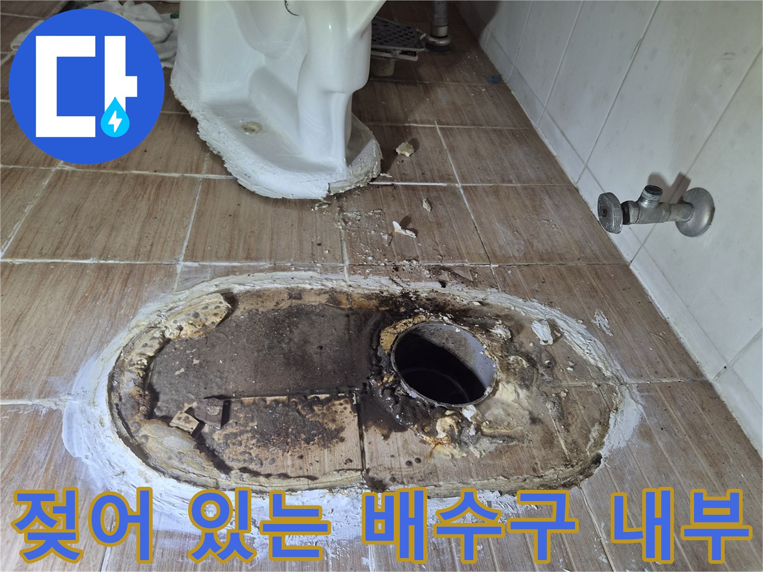 타일을 제거한 후 드러난 젖은 배수구 주변의 배관 모습입니다.