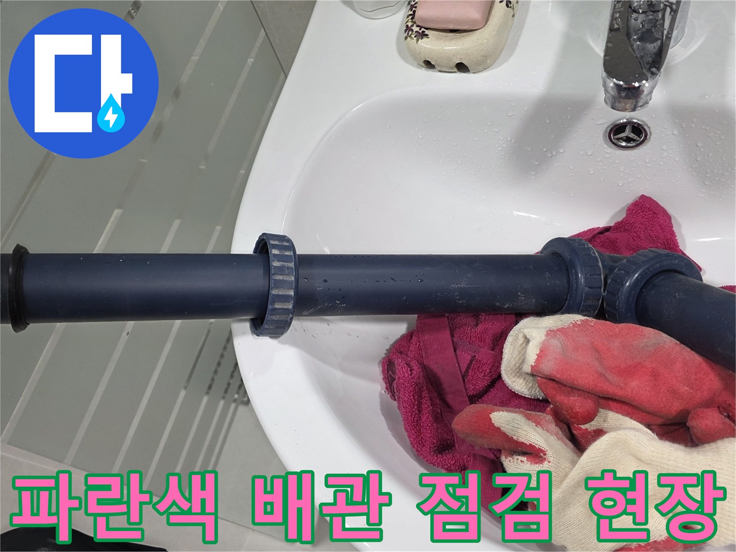 세면대 하단 파란색 배관과 작업용 장갑이 보이는 사진