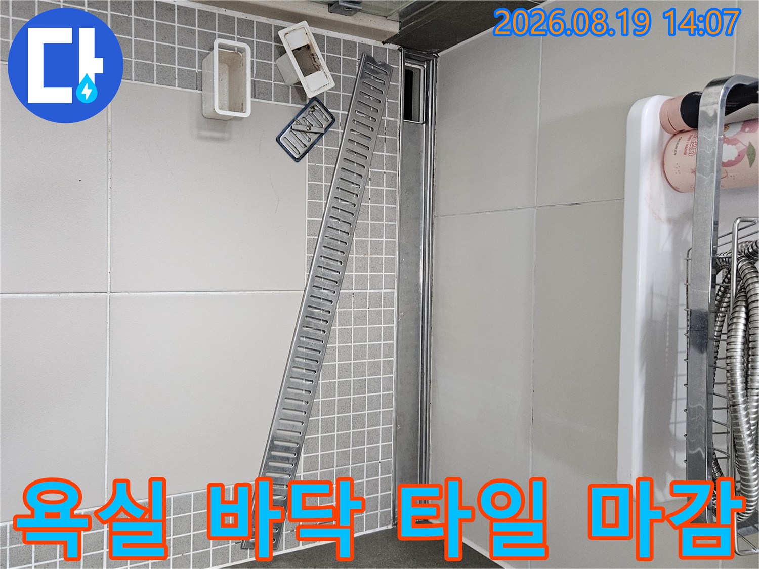 밝은 색상의 욕실 타일과 금속 배수 트렌치가 설치된 모습입니다.