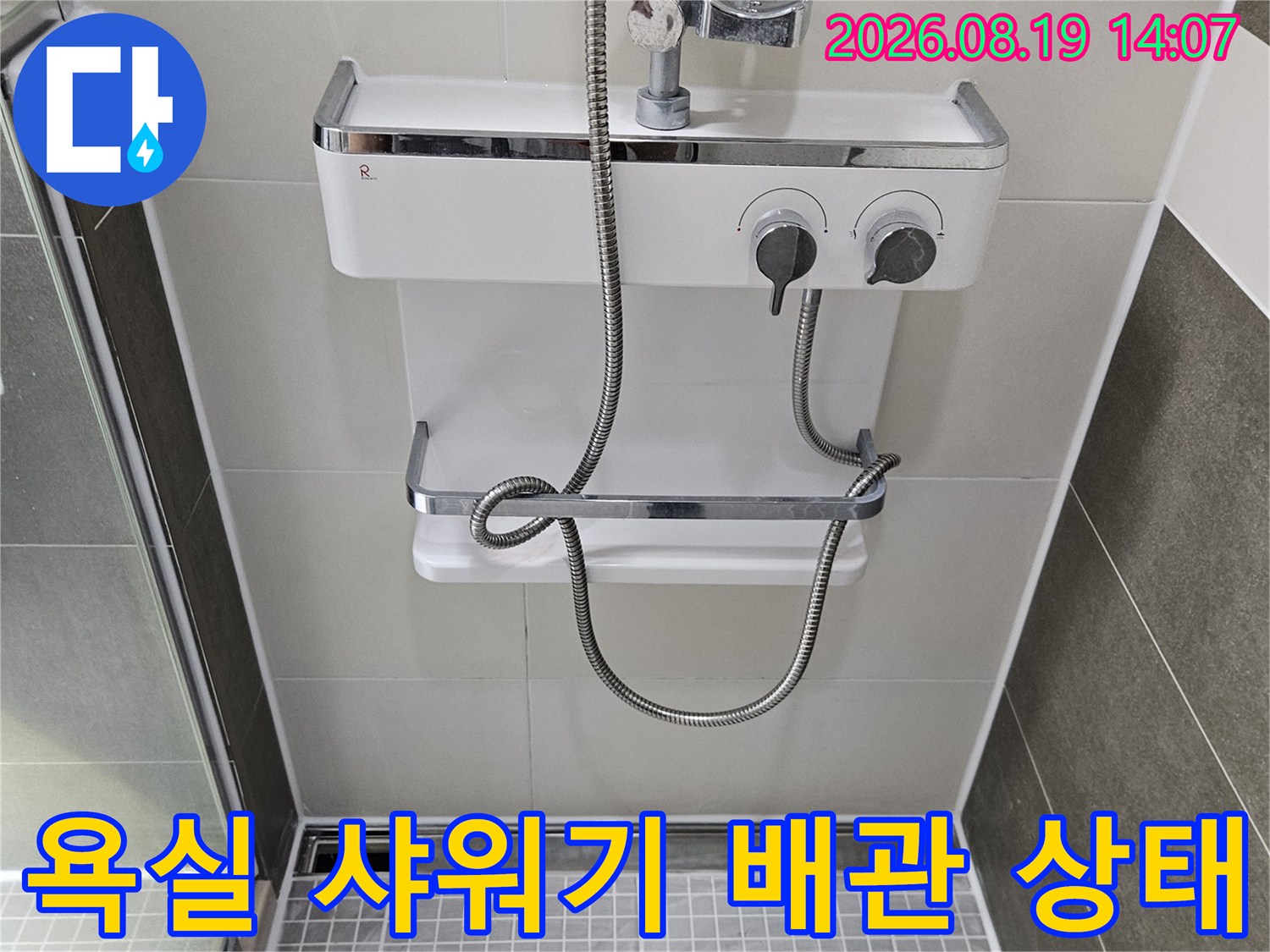 하얀색 타일 벽면에 부착된 샤워기 수전과 호스 연결 부위