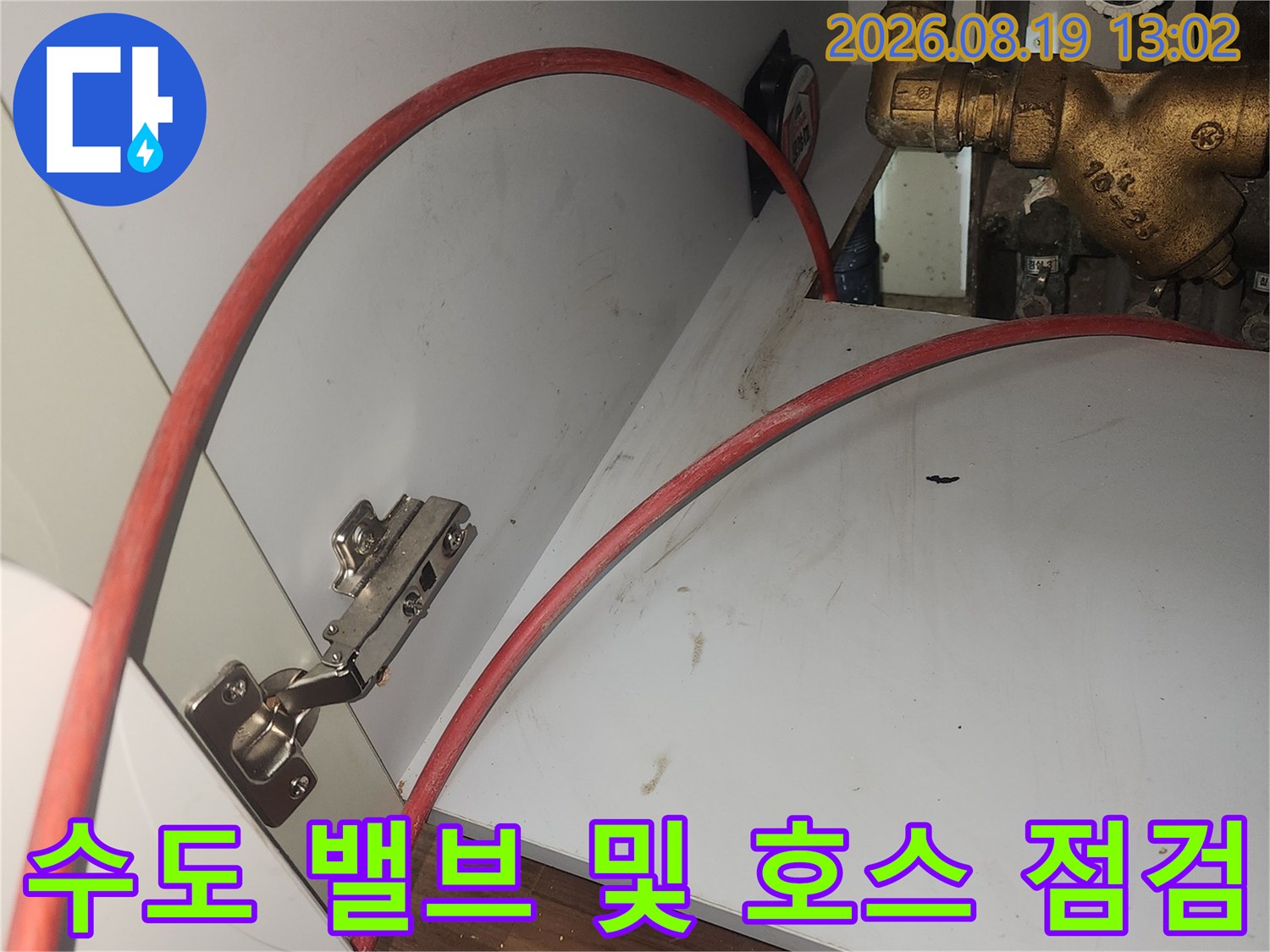 싱크대 하부의 금속 수도 밸브와 붉은색 급수 호스 모습