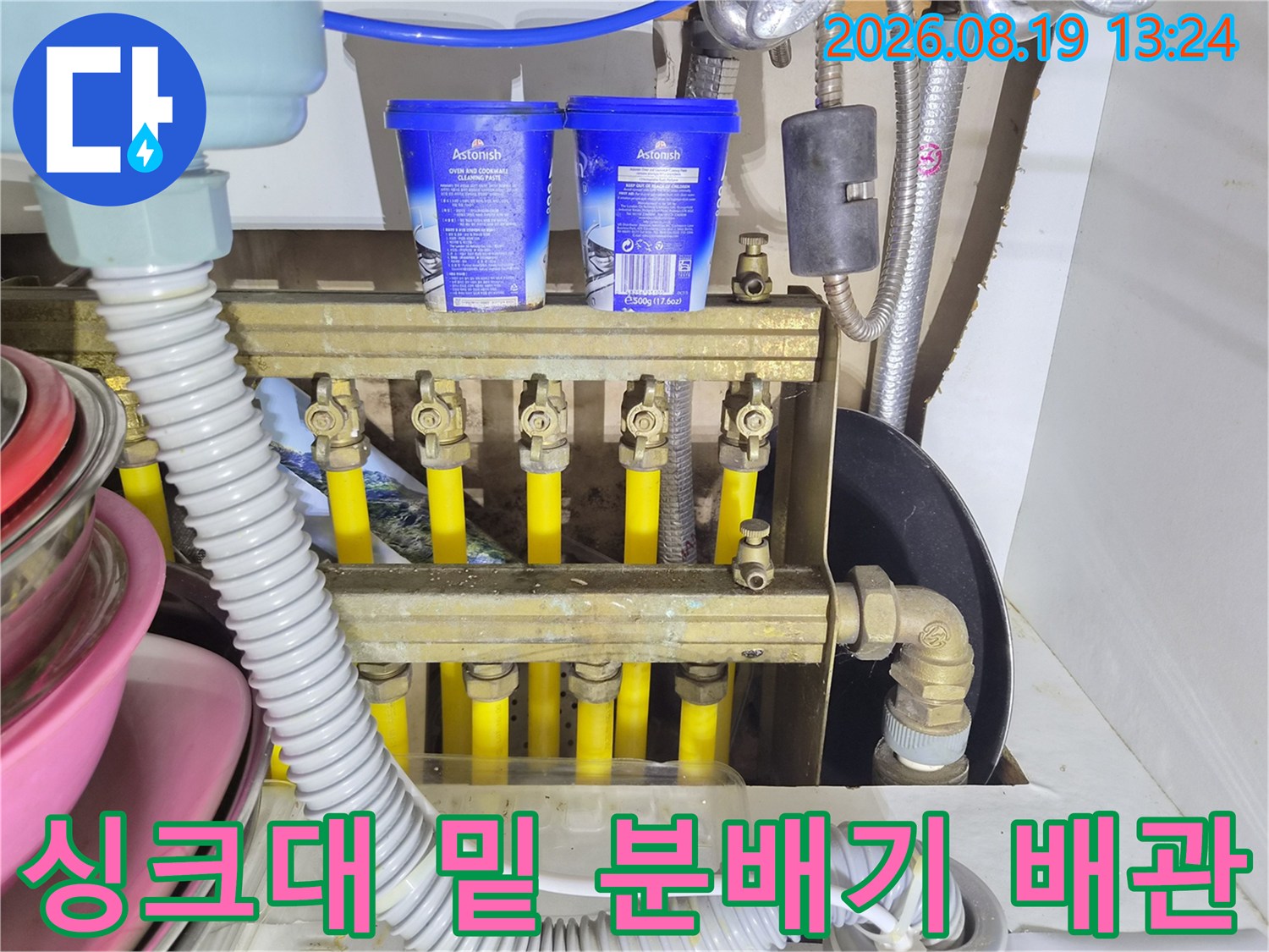 싱크대 하부장의 노란색 배관과 금속 밸브 장치를 보여주는 사진입니다.