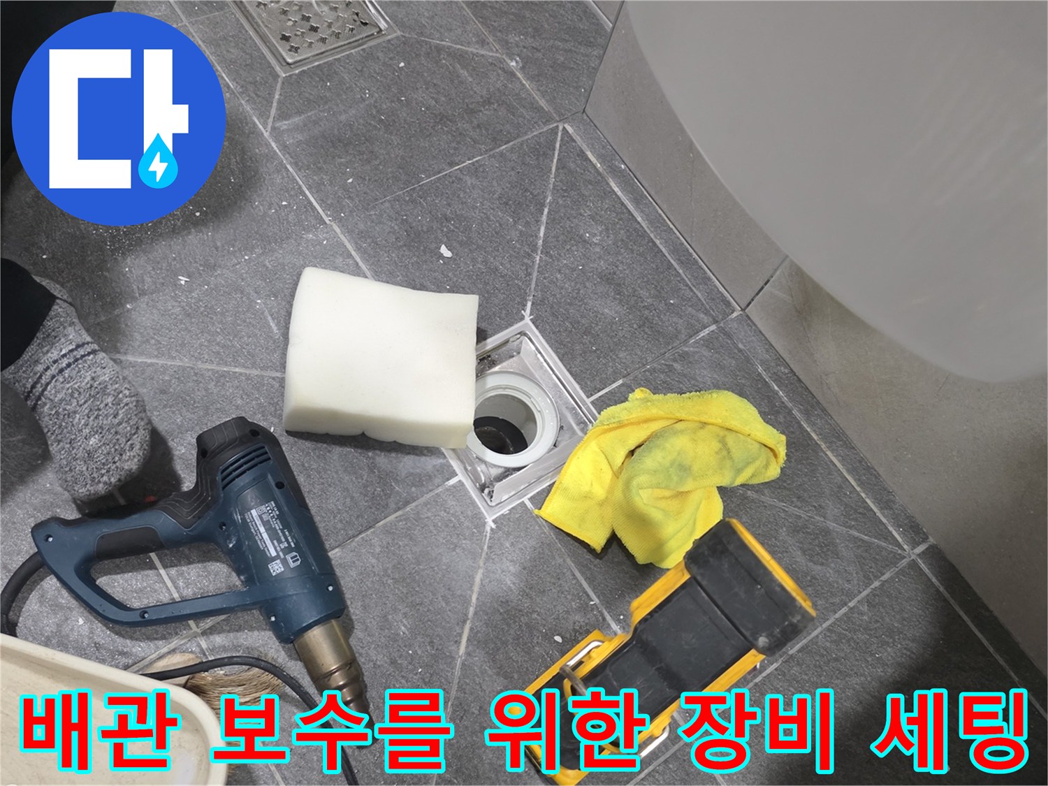 드릴과 청소 도구가 놓여 있는 욕실 바닥 배수구 주변의 작업 모습입니다.