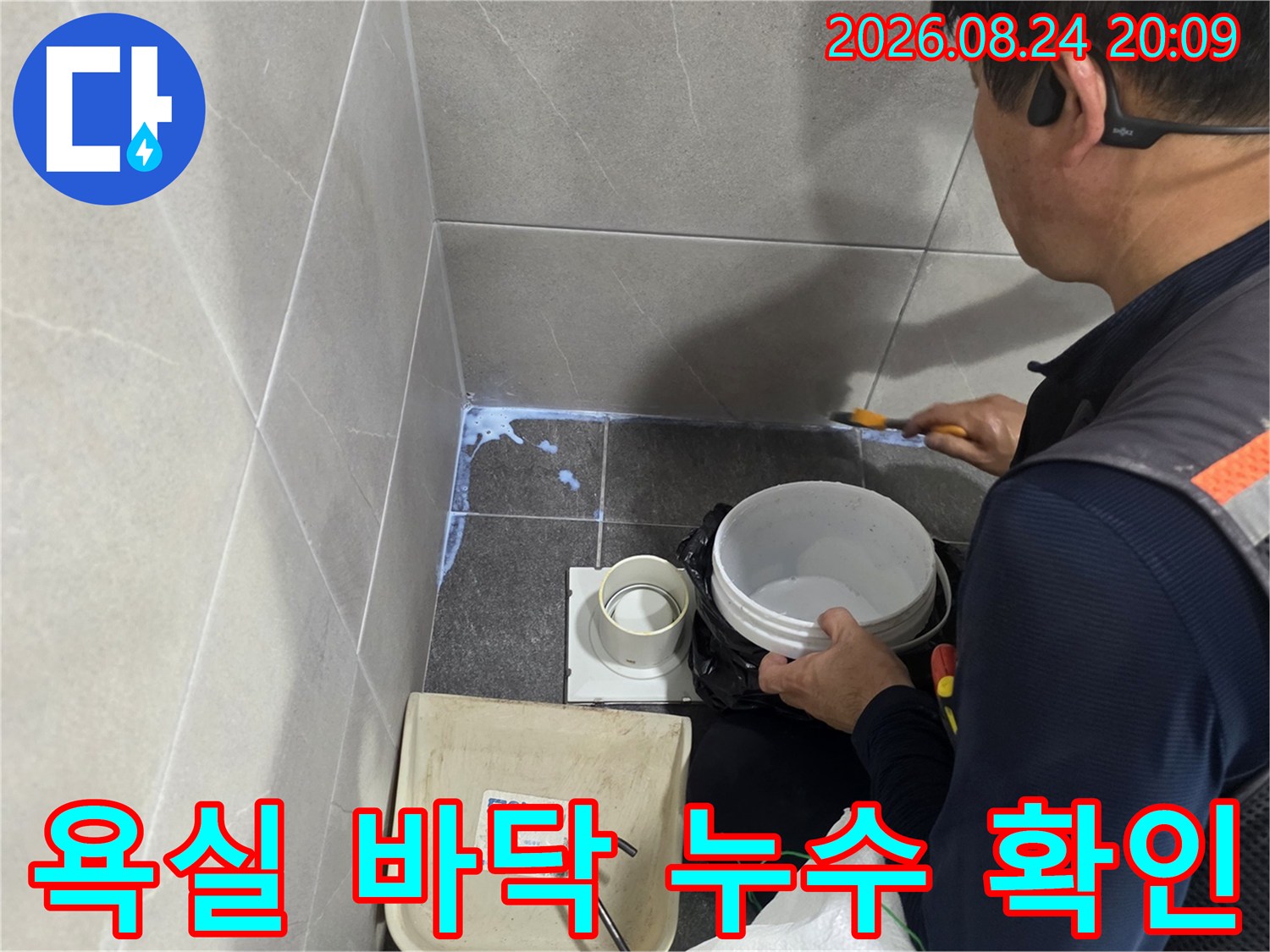 작업자가 욕실 배수구 주변의 타일 상태와 물기를 점검하고 있습니다