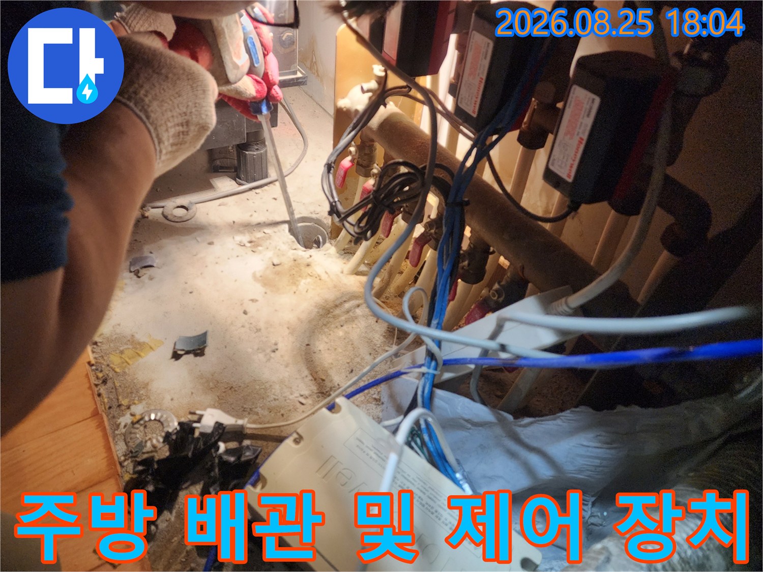 싱크대 하부의 배관 뭉치와 흰색 컨트롤러 박스 근접 촬영