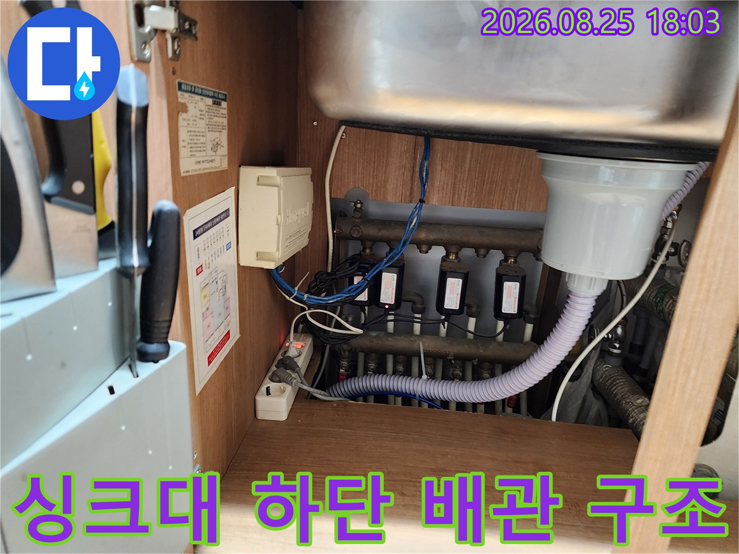 싱크대 하부장 내부의 흰색 주름관과 검은색 배관들이 연결된 모습