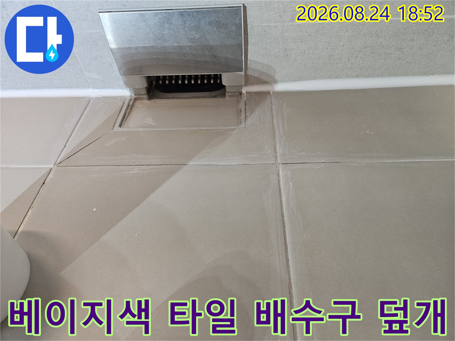 금속 소재의 배수구 트랩과 베이지색 욕실 타일의 접합부 상세 사진입니다.
