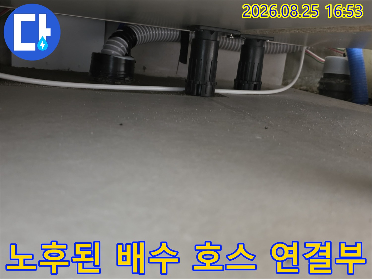 주방 싱크대 하단에 위치한 주름진 배수 호스와 검은색 배관 부품입니다.