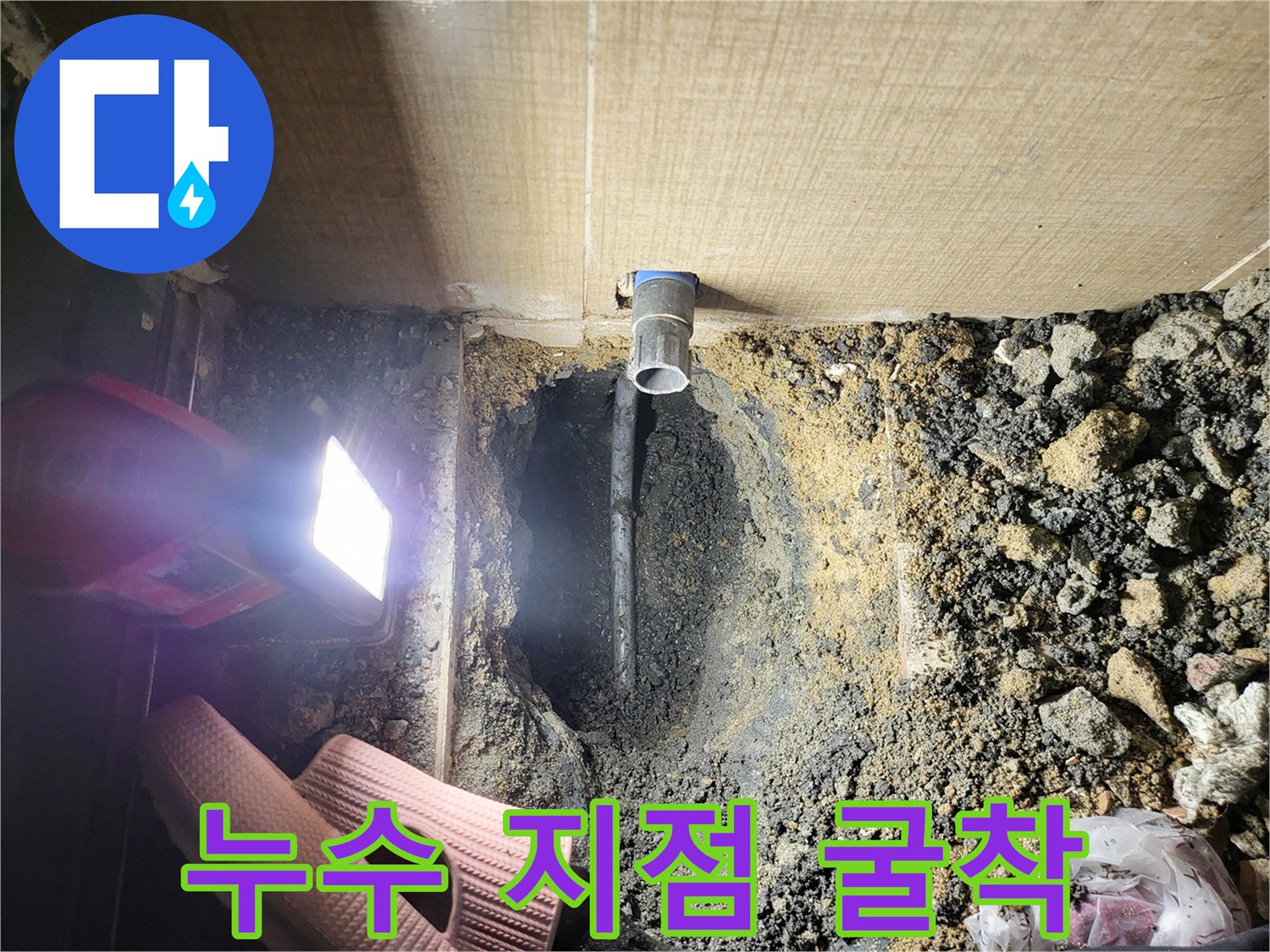 손전등으로 비춘 배관 주변의 습한 흙과 파란색 관