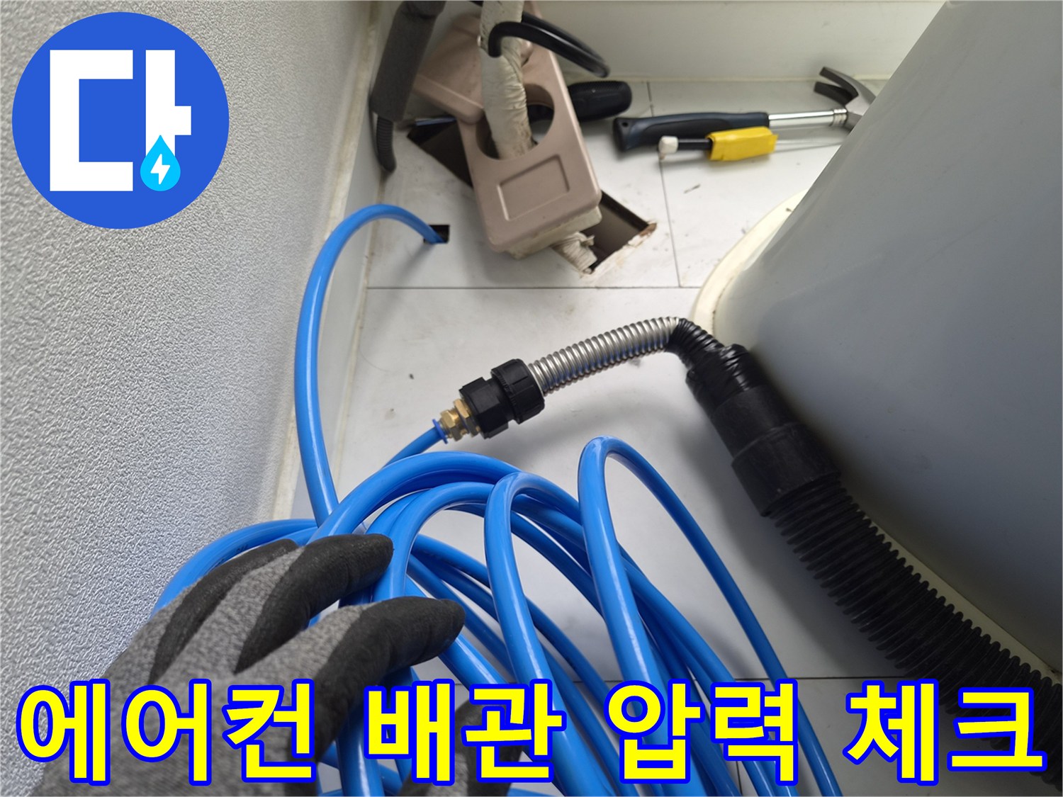 파란색 호스가 연결된 은색 주름관과 작업자의 장갑 낀 손