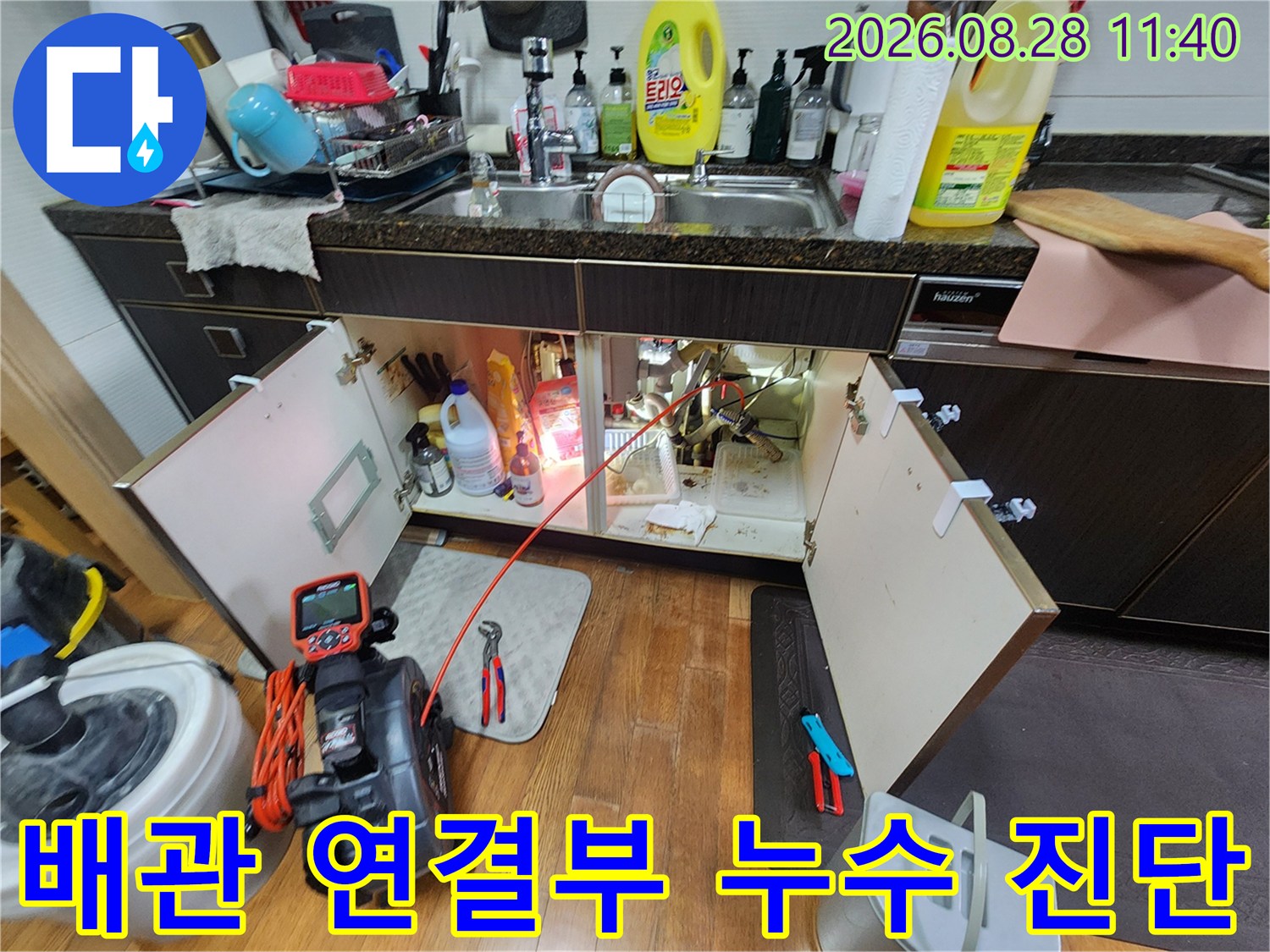 싱크대 하부장 내부의 배관 틈새와 연결 부위를 조사하며 누수 지점을 추적하는 작업 장면입니다.