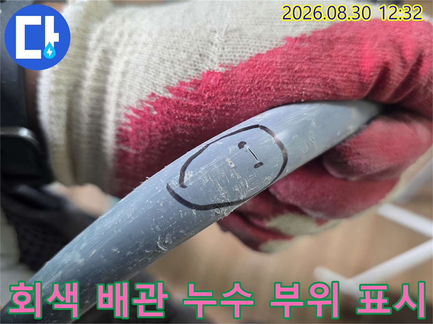 작업자의 장갑 낀 손이-회색 배관의 누수 지점을 가리키고 있습니다