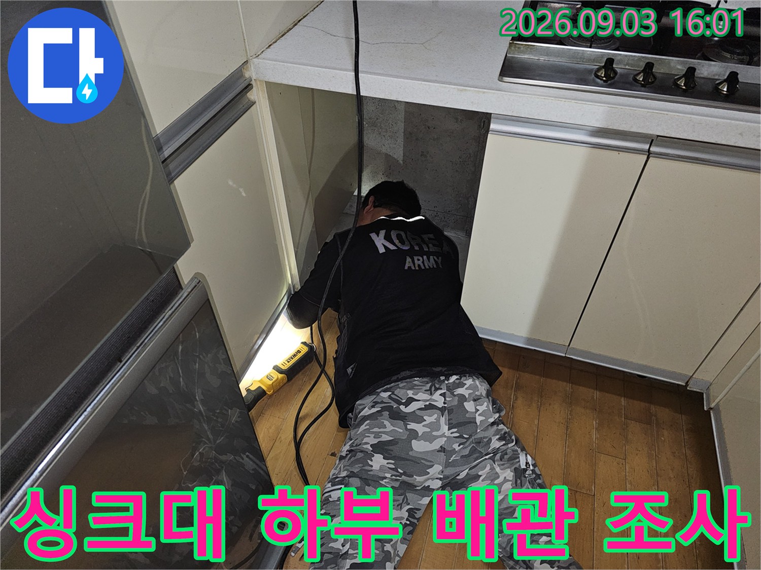 싱크대 밑 좁은 공간에서 조명을 비춰 배관을 점검하는 장면입니다.