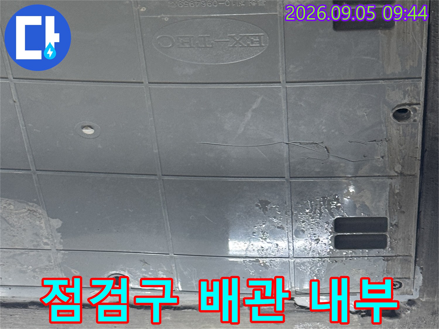 점검구 내부에 위치한 배관과 젖은 벽면을 근접 촬영한 사진입니다.