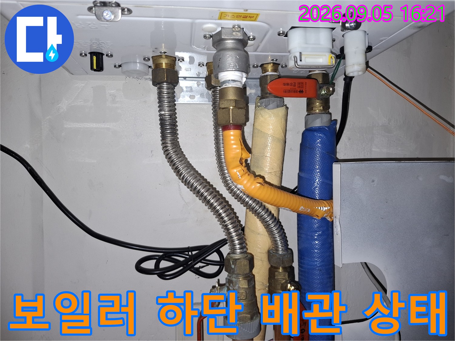 보일러 하단의 금속 관과 보온재 처리된 배관의 연결 부위를 촬영했습니다.