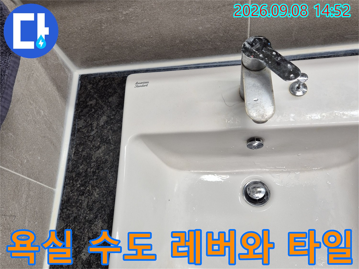 금속제 수전 핸들과 회색 벽면 타일의 근접 사진입니다.