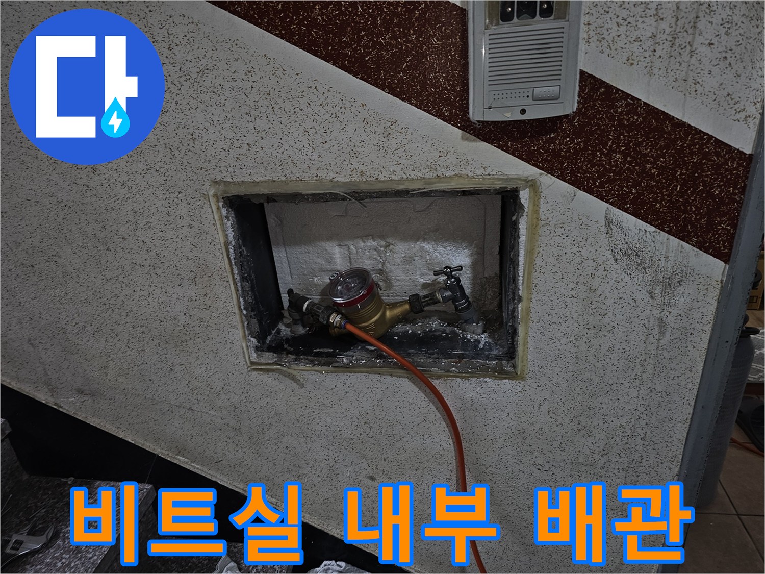 벽면 타공 부위로 보이는 계량기 장치와 점검용 호스 연결 모습
