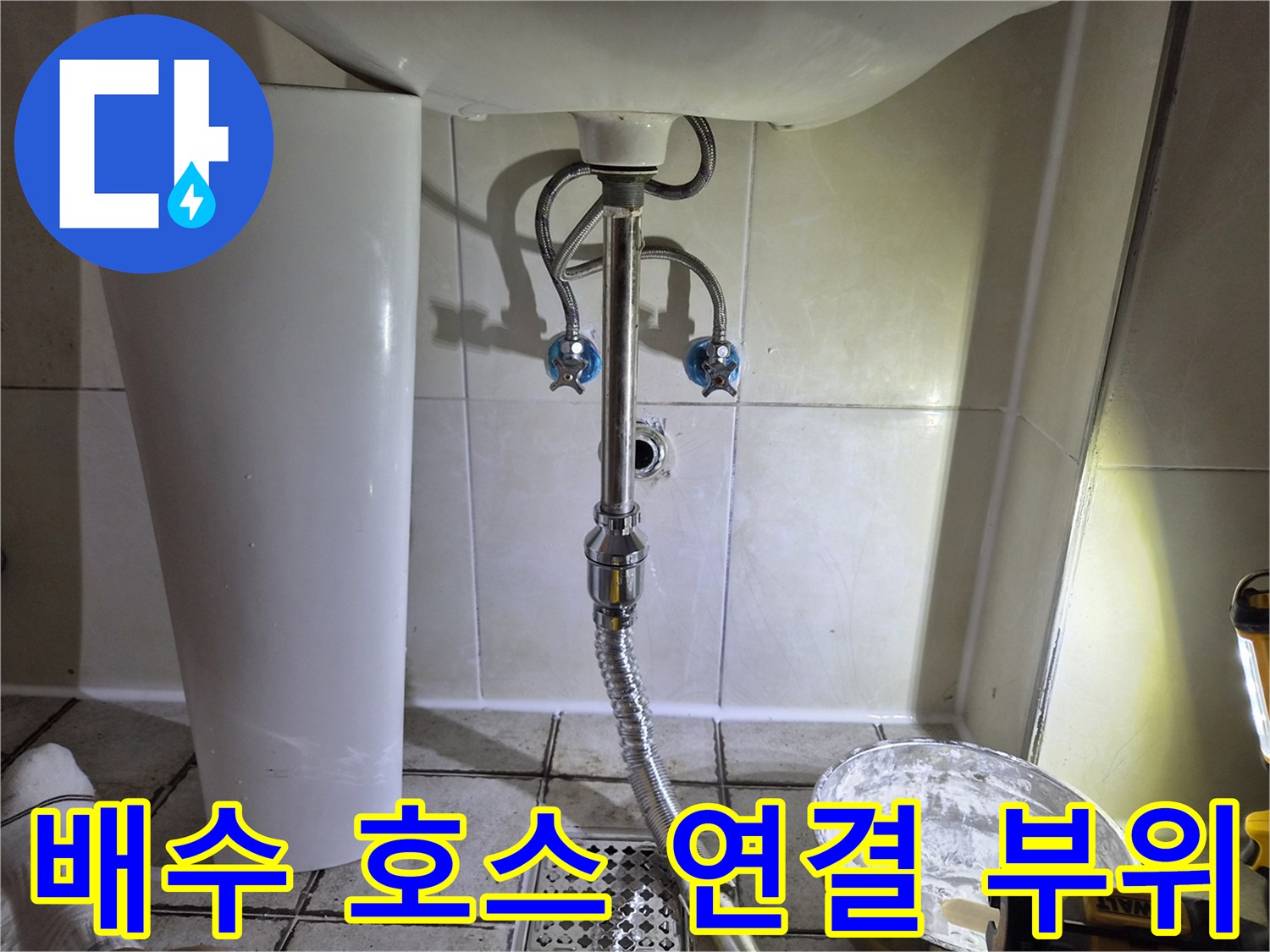 세면대 아래 은색 자바라 호스와 벽면 타일 상세 모습