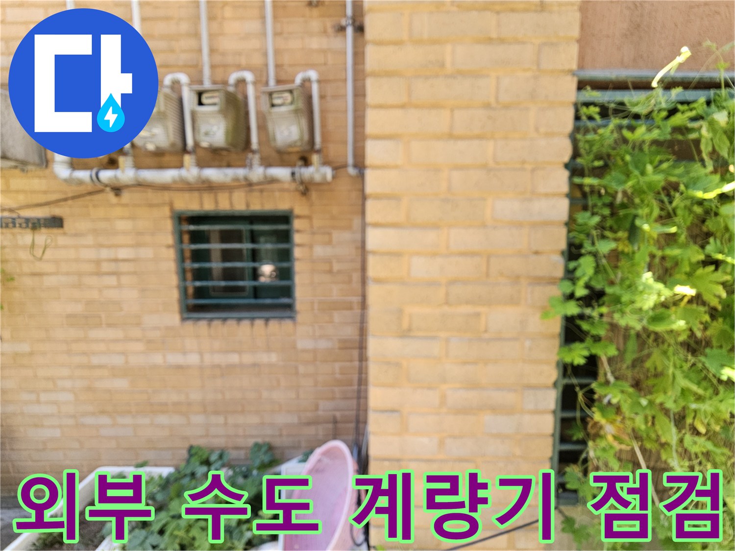건물 외벽 황색 벽돌에 설치된 수도 계량기와 상단 노출 배관