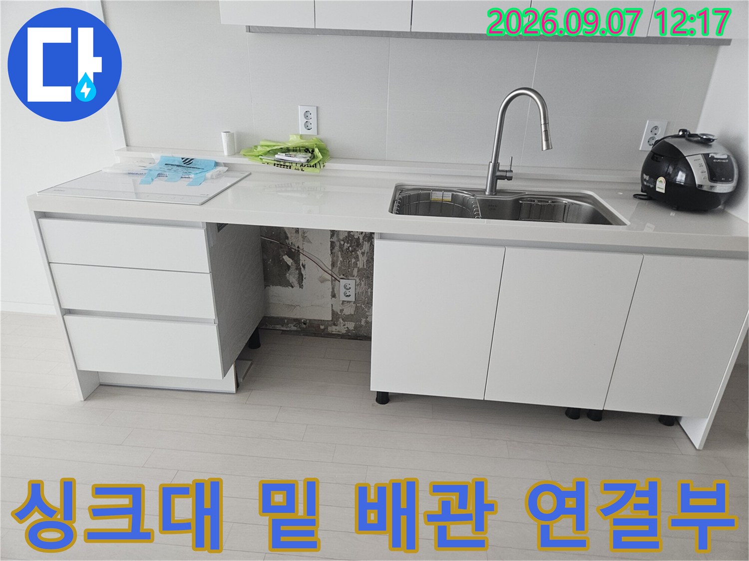싱크대 아래쪽 훼손된 배관과 테이프로 고정된 부위의 근접 사진입니다.