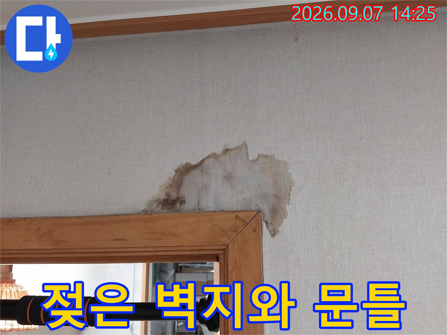 나무 프레임 상단에 넓게 퍼진 누수 얼룩 및 젖은 벽지 모습입니다.