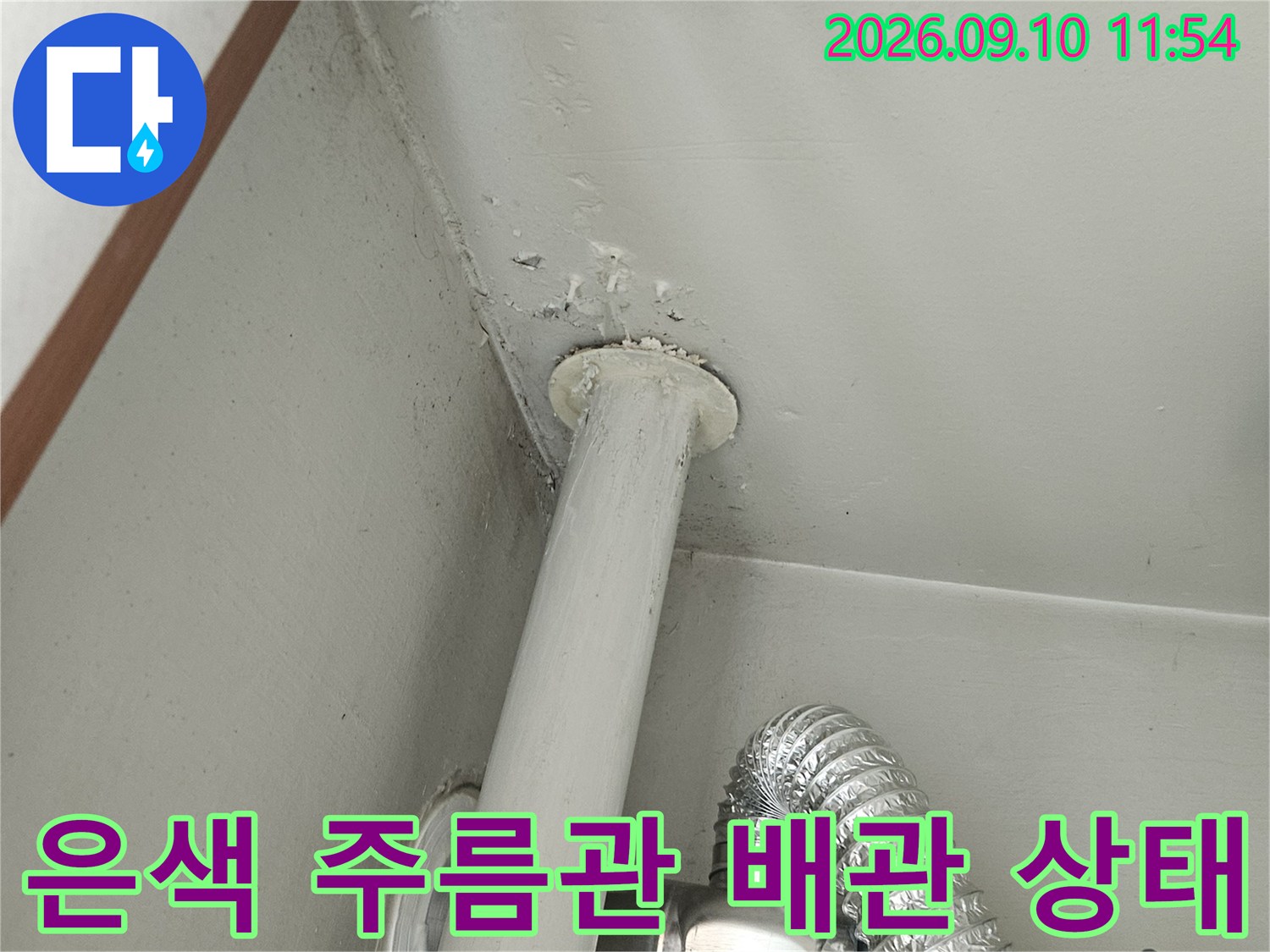 천장 내부에 설치된 은색 주름관과 흰색 수직 배관의 연결 모습입니다.