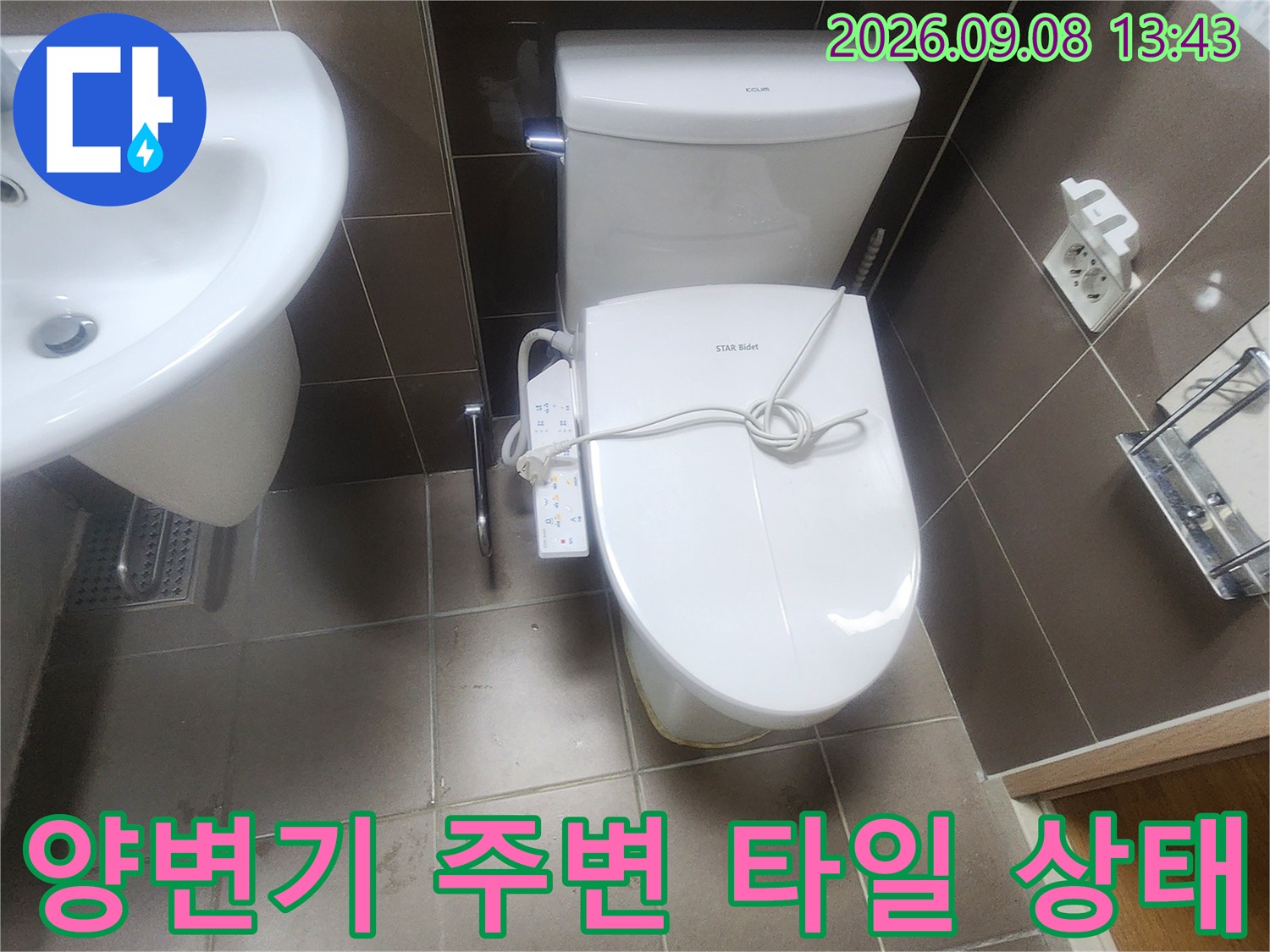 베이지색 타일 바닥에 설치된 하얀 양변기와 주변 배관 연결 부위