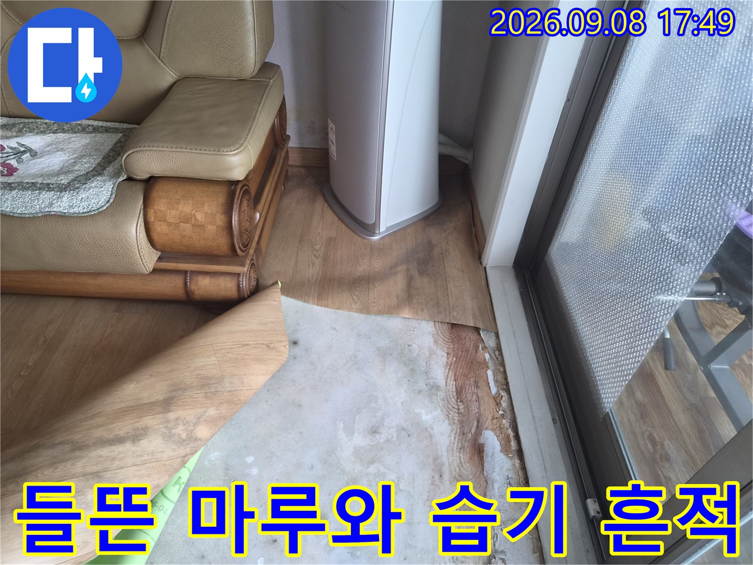 거실 소파 옆 바닥 마루가 들뜨고 습기가 스며든 상태의 사진
