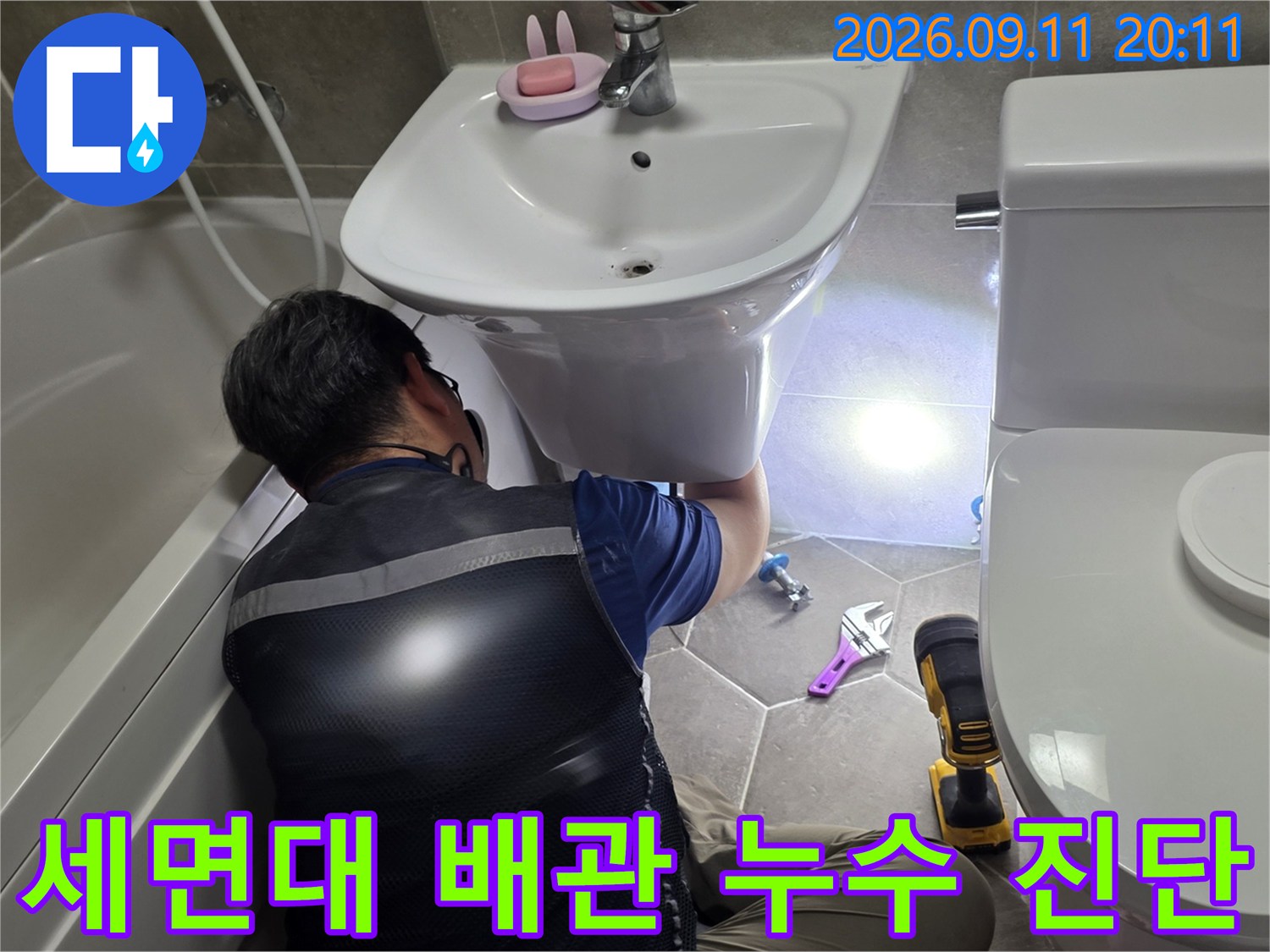 욕실 세면대 하부의 배관 연결 상태를 점검하고 있는 전문 엔지니어의 작업 모습