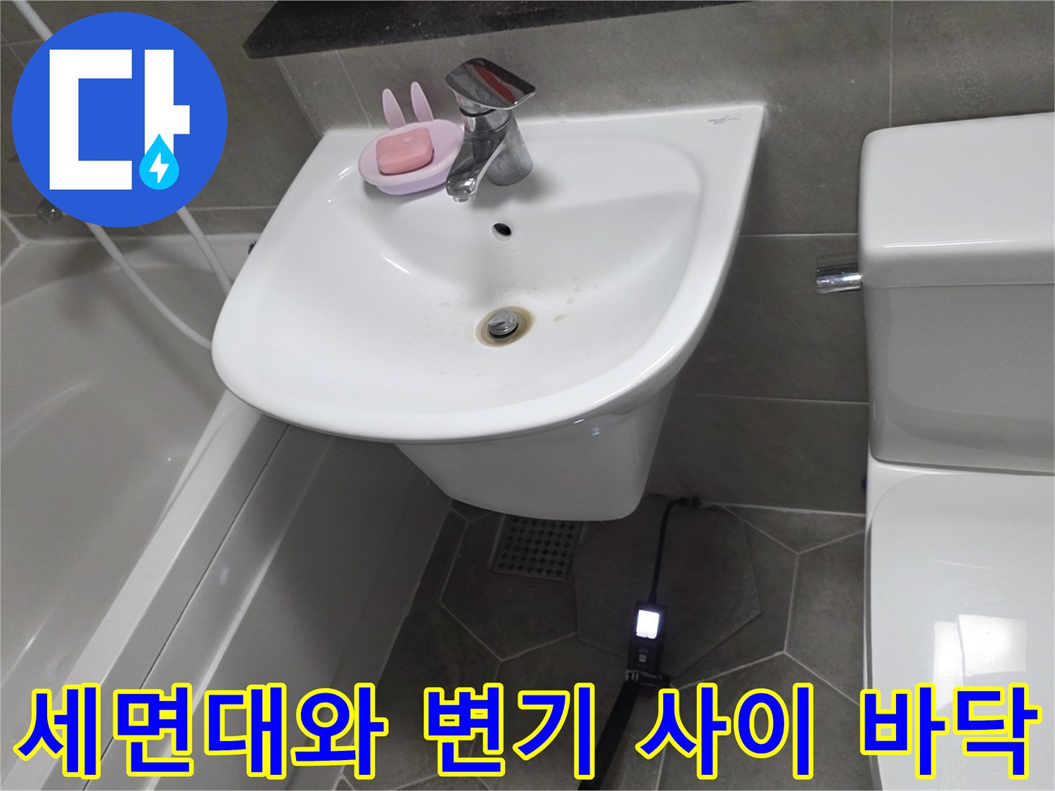 화장실 세면대 아래쪽 타일과 배관 주변의 상태를 보여주는 사진