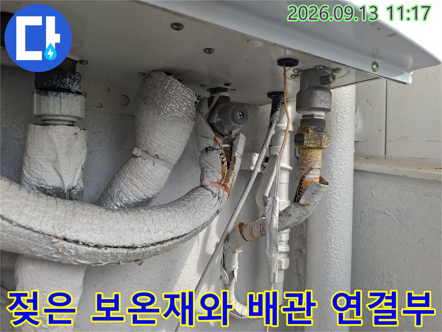 습기를 머금어 변색된 배관 보온재와 금속 연결 부위의 근접 촬영입니다.