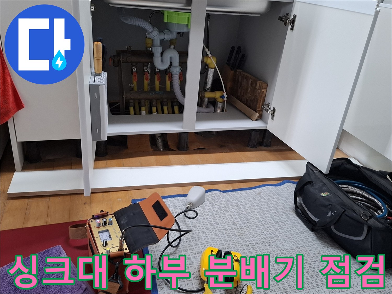 싱크대 하부장 내부의 난방 배관 분배기와 검사 장비 모습