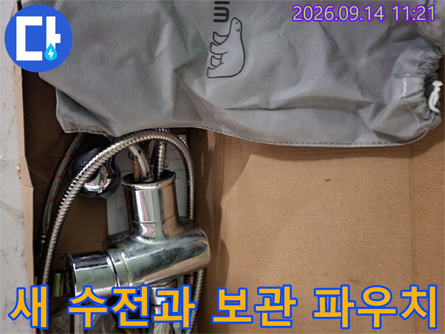 상자 안에 놓인 샤워기 본체와 회색 천 파우치