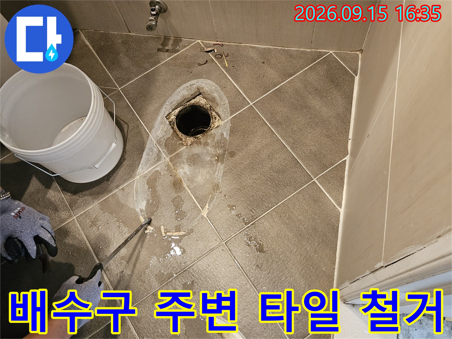 화장실 바닥 배수구 주변의 파손된 타일을 제거하고 내부 배관을 확인하는 모습입니다.
