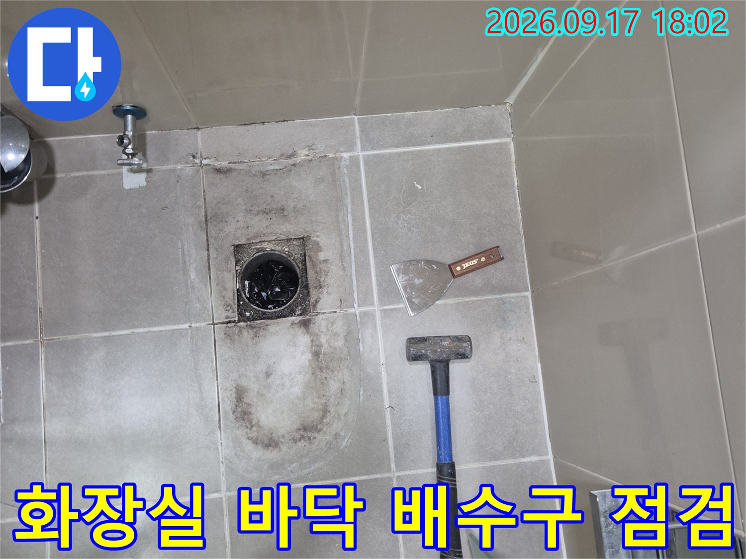 망치와 헤라가 놓인 화장실 바닥의 훼손된 배수 트랩 주변 모습입니다.
